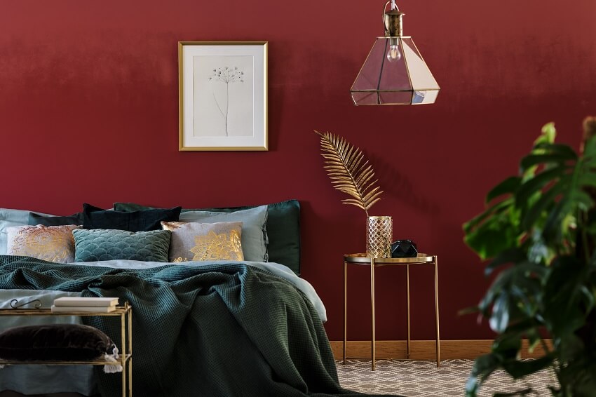 Maroon painted wall in bedroom with golden furniture 