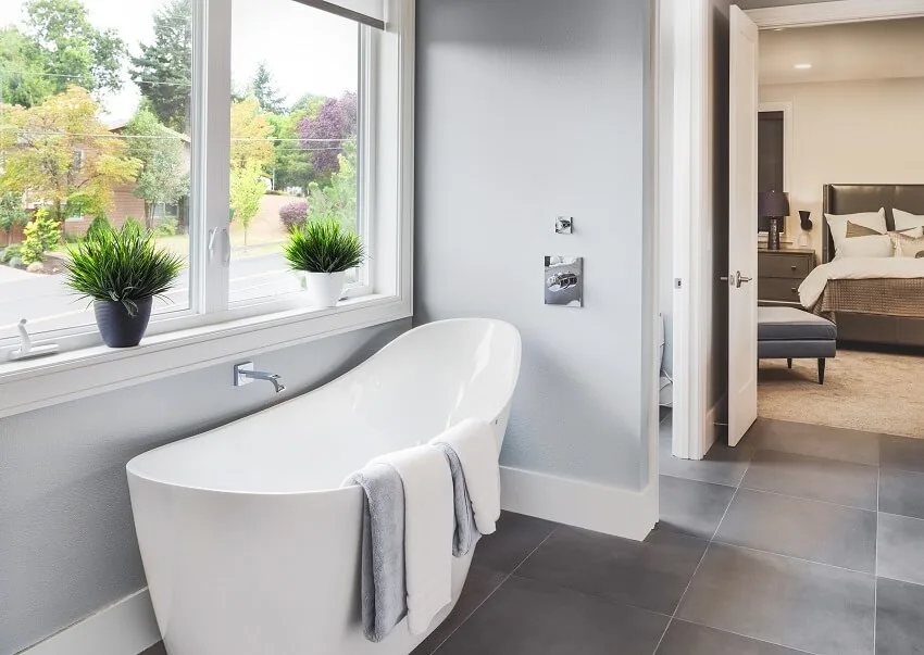 Master bathroom with bath tub grey tile floor glass windows and view of master bedroom