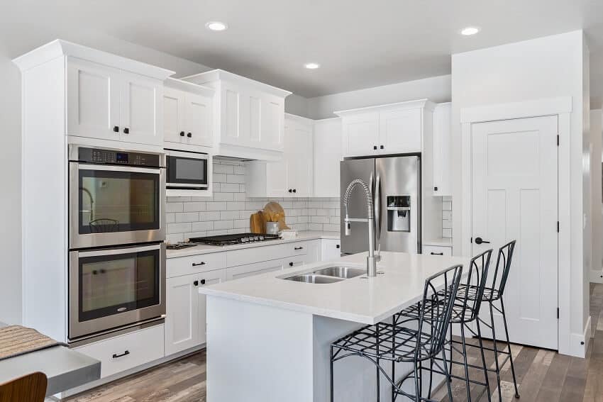 Metal stools stainless steel double oven and french door refrigerator in white kitchen with staggered cabinets