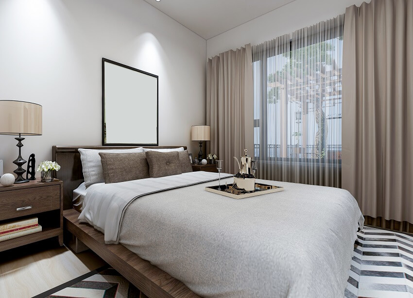 Modern bedroom with mirror lampshades and decors on bedside table tray with pitcher and glasses on large bed in linen sheets and black and white carpet