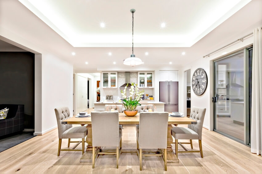 Modern dining room with hanging lamps on cove ceiling and dining set with fancy items on the wooden floor