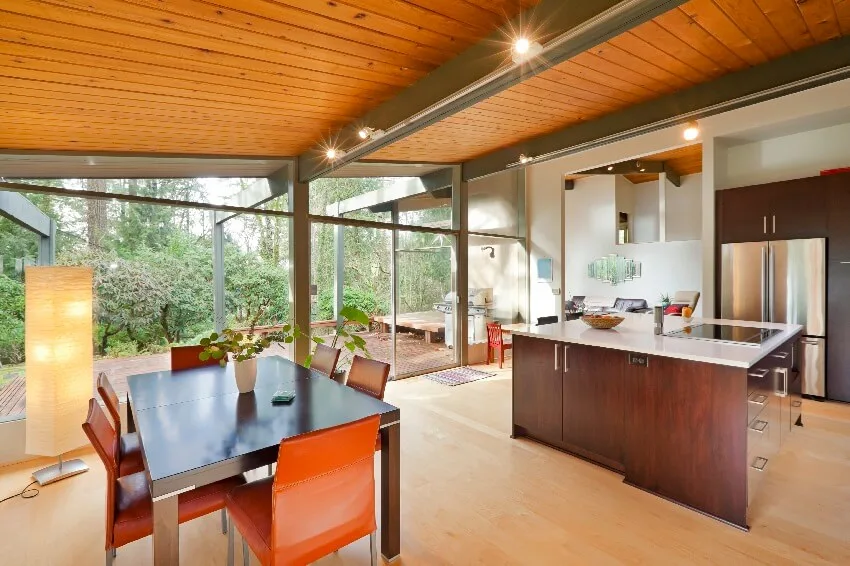 Modern kitchen and dining area with metal posts and beams wooden floor and ceiling in a glass house