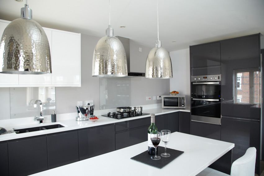 Modern kitchen with black cabinets white backsplash countertop center island hanging dome shaped lights oven