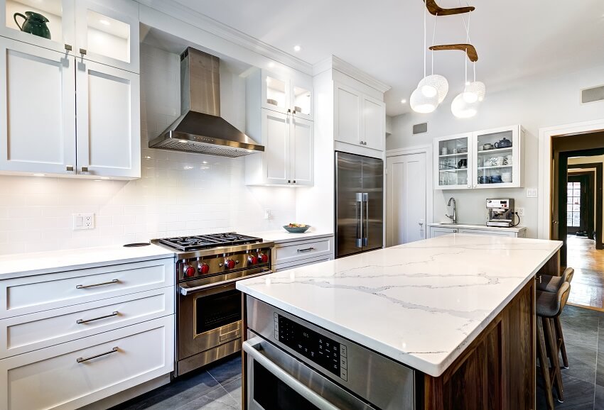 Modern kitchen with marble island white cabinets stainless steel appliance pendant lights barstools and grey tile flooring