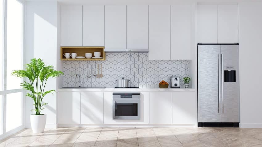 Modern white kitchen with stainless steel appliances staggered cabinets and potted indoor plant