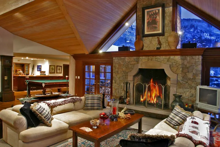 Mountain vacation house interior fireplace antiques on ledge wooden ceiling couch table entertainment room