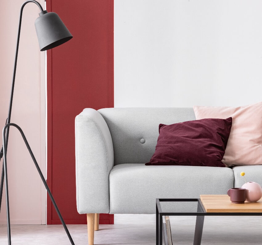 Pastel pink and burgundy cushions on grey sofa in living room with maroon pink and white wall and modern black lamp