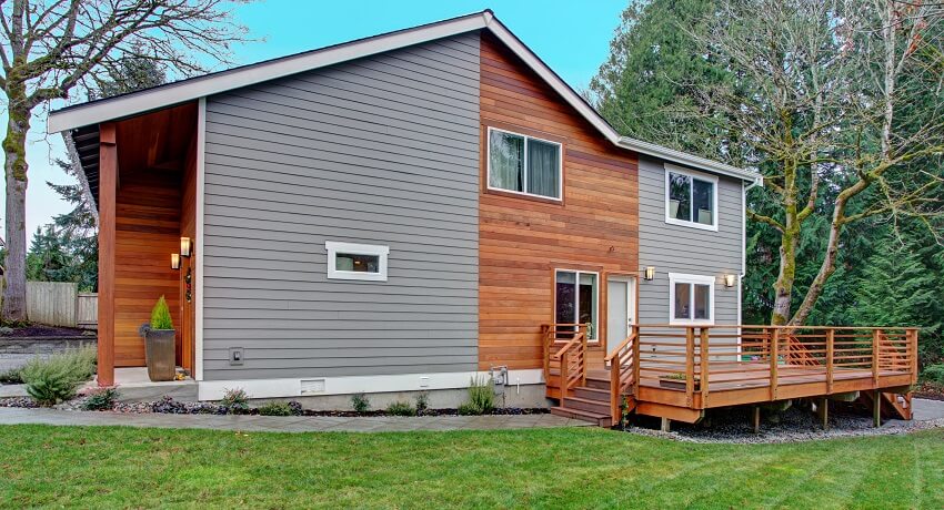 Renovated home exterior with natural wood and grey siding walk out deck with wooden handrails and green lawn
