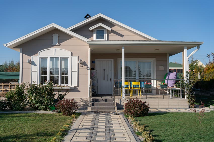 Bungalow with paved walkway, yellow outdoor chair and porch with windows
