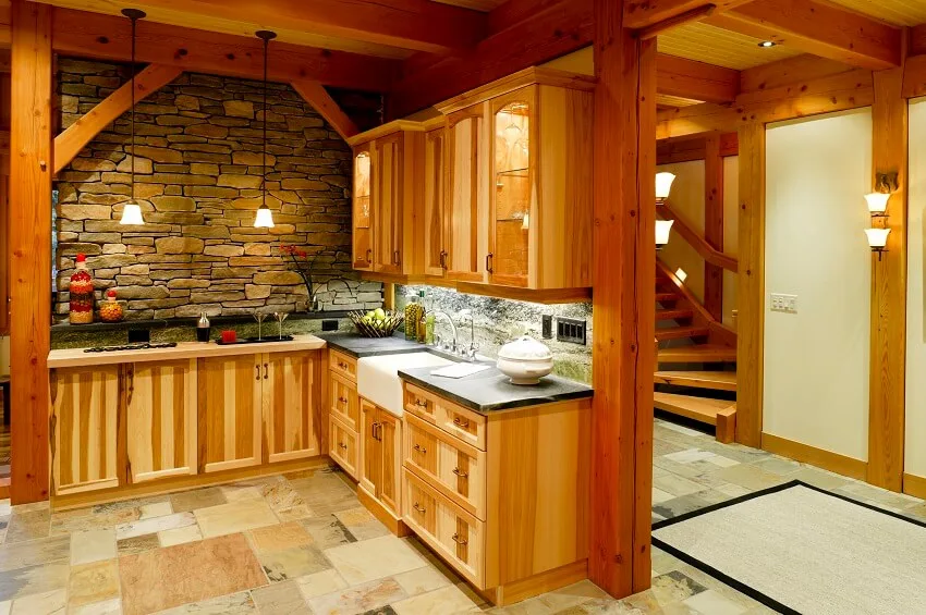 Small kitchen with stone floors and wall wooden cabinets light fixtures post and beam and view of a staircase