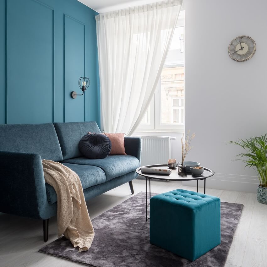 Small living room with teal blue wall with decorative molding modern sofa black coffee table and square quilted ottoman