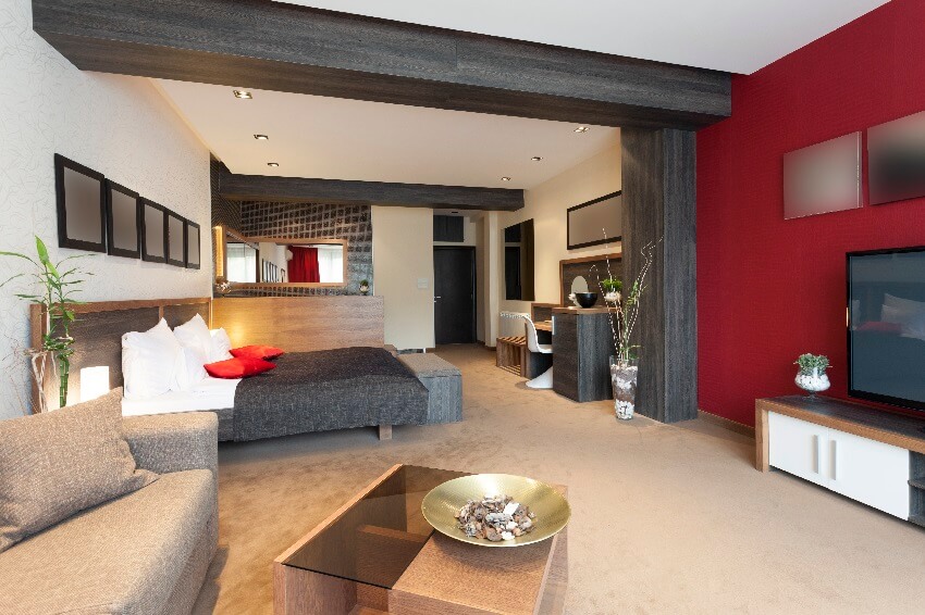 Spacious hotel room with with bed sofa, post & beam and white & maroon color walls