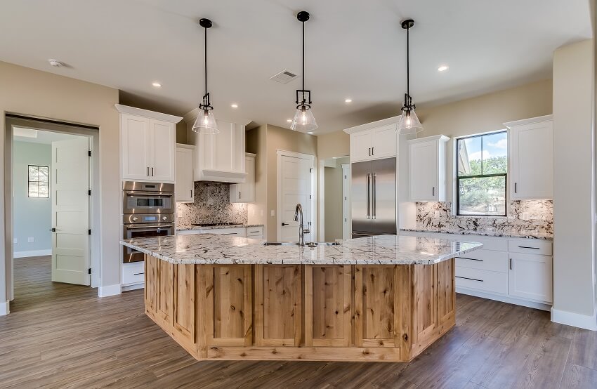 Three pendant lights hang over island with stainless steel appliances fixtures and natural wood look on island and flooring