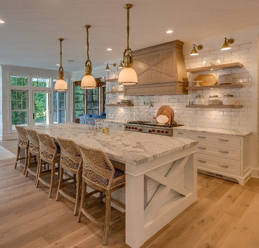 Three pendant lights hang over the island with busy granite countertop decorative vent hood over the stove