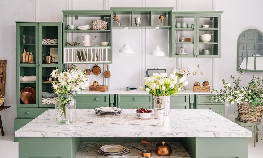 Vintage designed green kitchen with flowers in metal bucket on artificial marble counter cabinets and open shelves with kitchen essesntials
