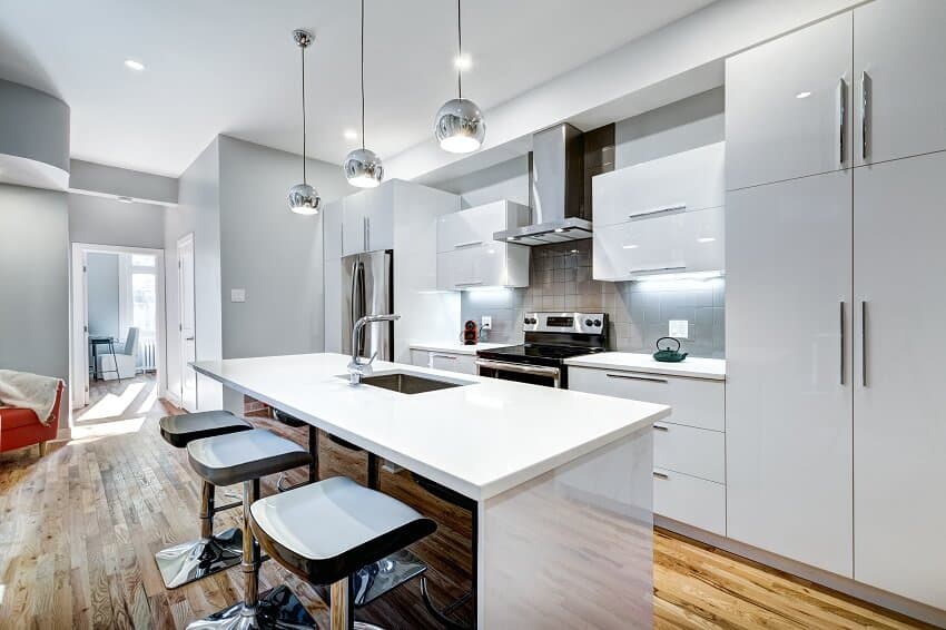 White kitchen with island and chairs, wooden floors, pendant lights and staggered cabinets
