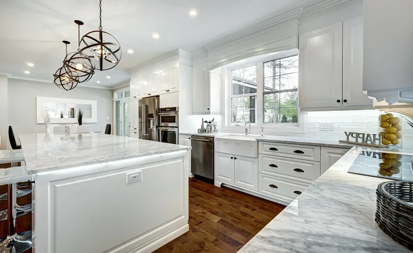 White kitchen with windows island marble countertop cabinets stainless steel appliance pendant lights barstools and hardwood floors is