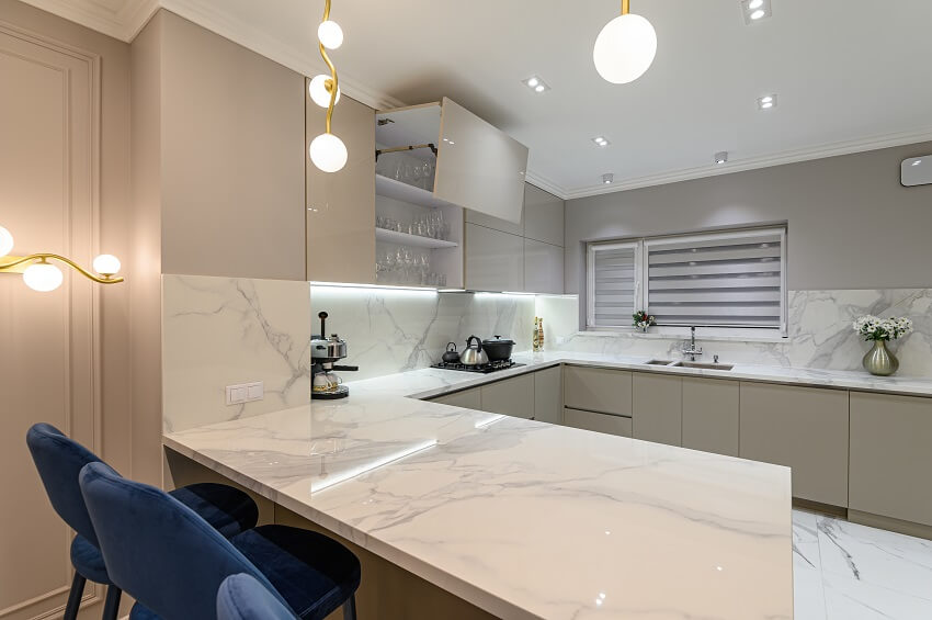 White modern kitchen with artificial marble countertop cabinets lighting fixtures and blue bar stools