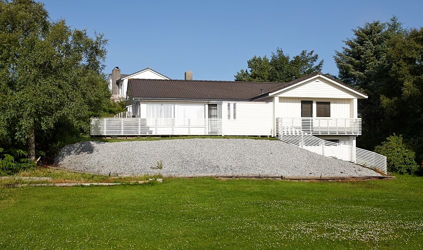 White elevated wooden ranch house with horizontal white ornamental fence and large open yard