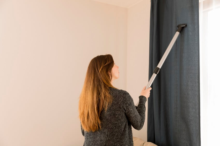 Woman cleaning blackout curtain with vacuum cleaner