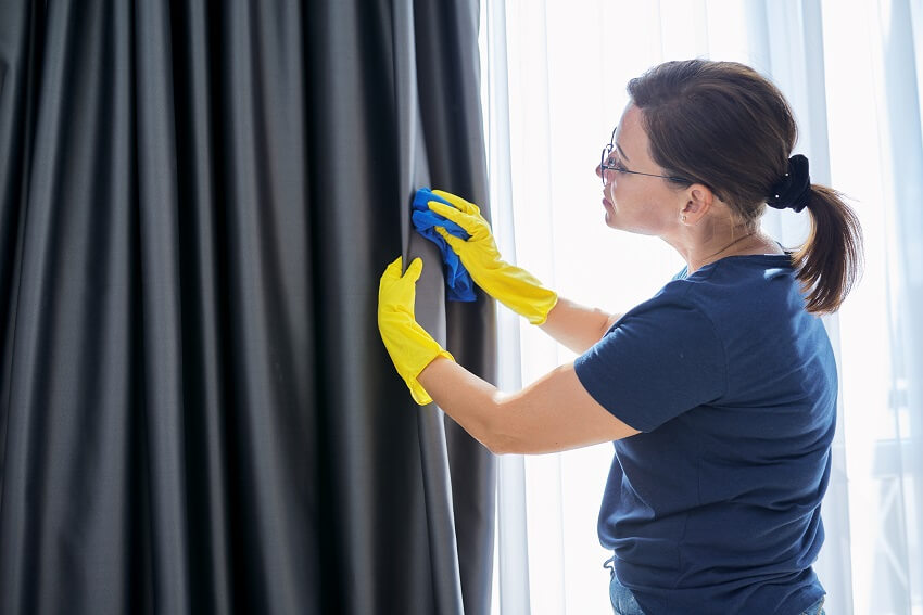 Woman in gloves with a rag cleaning silk blackout curtains