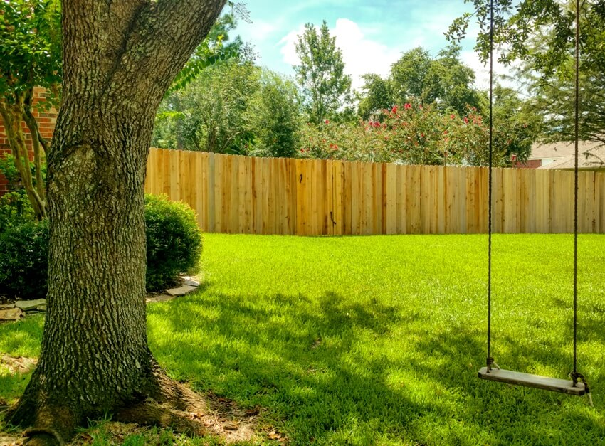 Wooden rope swing hangs in the shade of an oak tree in a private lawn 