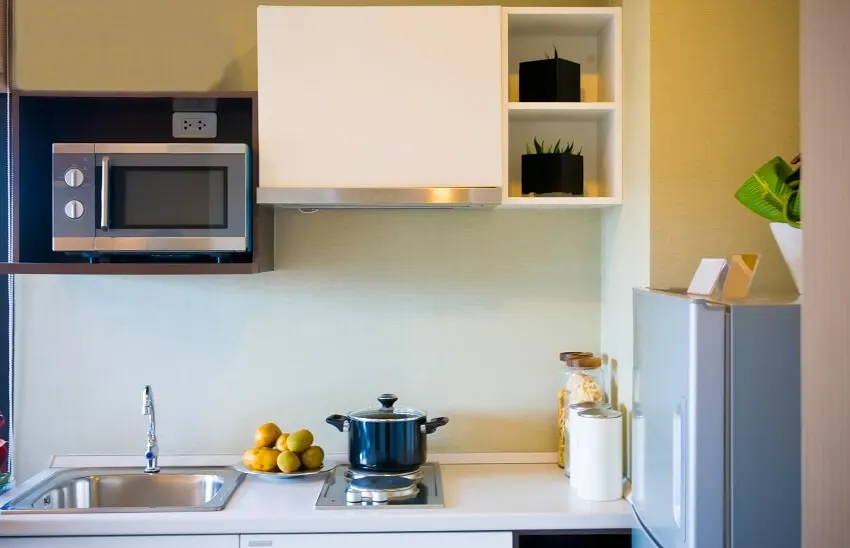 Residential interior of a small modern kitchen with microwave cooktop with pot on a white counter a sink and a small fridge