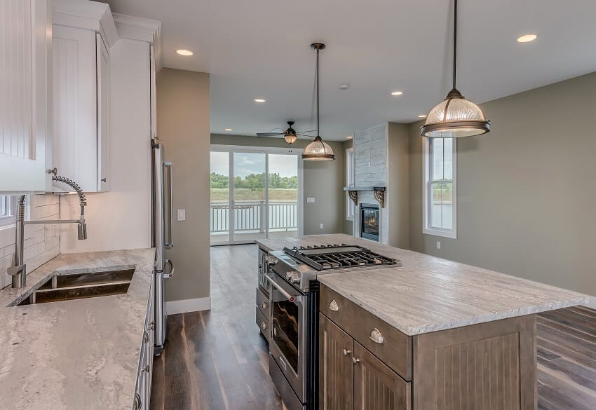 Empty open space kitchen with two pendant ligths hang above kitchen island range brick backsplash hardwood floors grey walls and honed marble countertops