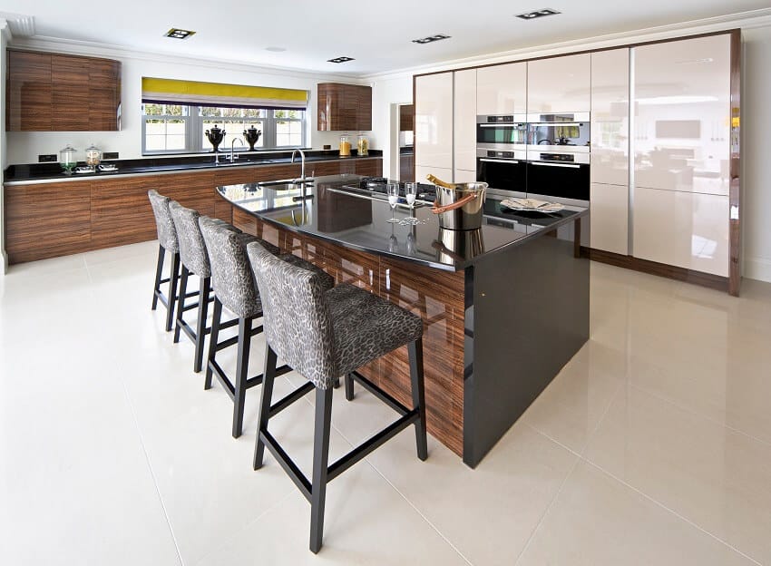 A bright and spacious kitchen with white tile floors cabinets with wood design wallpaper and a large island with a black granite countertop and bar stools