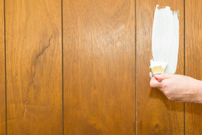A house painter's hand applying primer to wood paneling