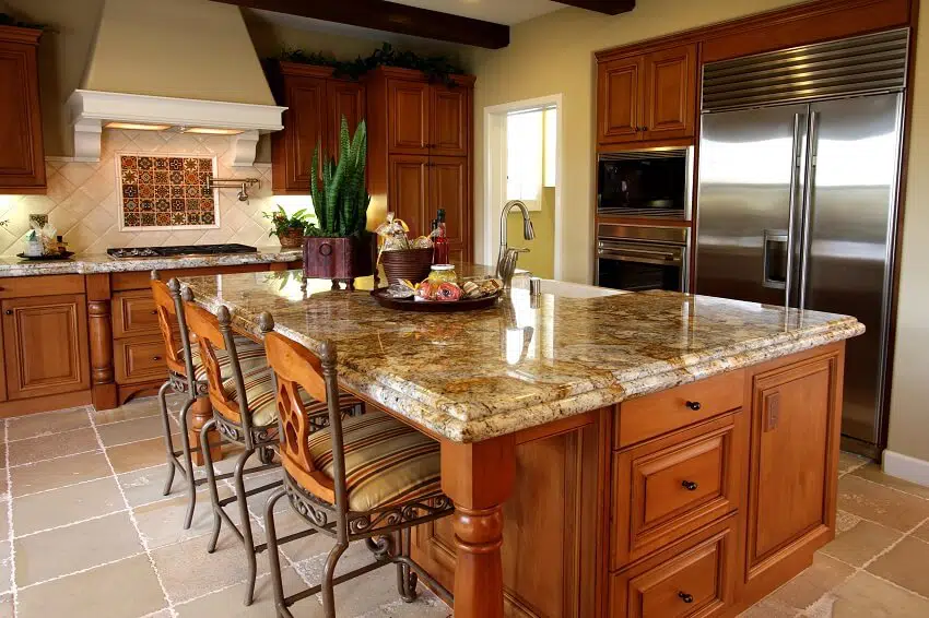 A kitchen with granite counters tile backsplash tile floors stainless steel appliances and a huge island with chairs built in drawers and cabinets and decors on top