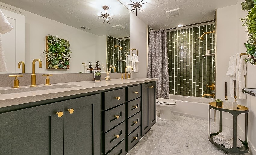Basement bathroom with green tile in the shower area brass faucets and fixtures hexagon tile floors large mirror and green cabinets and drawers