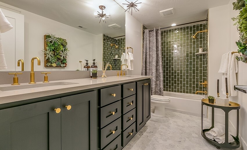 Basement bathroom with green tile in the shower area brass faucets and fixtures hexagon tile floors mirror and green cabinets and drawers