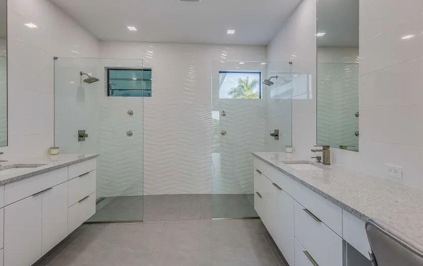 Bathroom with a doorless walk in shower with double shower heads two vanities white cabinets and grey tile floors