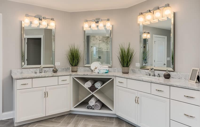 Bathroom with white cabinets three mirrors with lighting fixture above grey walls and marble counter tops