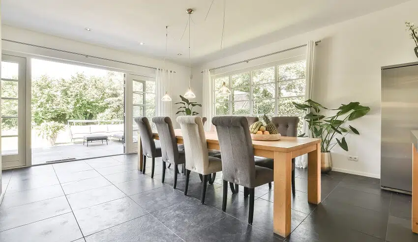 Beautiful dining room in natural light with dark grey tile floors wood dining table grey and cream colored chairs large windows and huge open doors