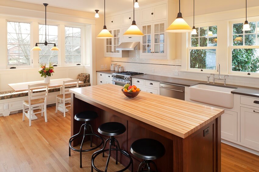 Beautiful kitchen with brown countertops, dining table with bench, island with bar stools and wood floors