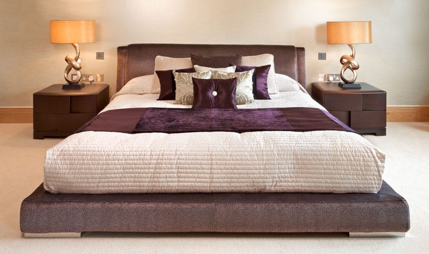 Bed with purple sheets and pillows nightstand lamps headboard