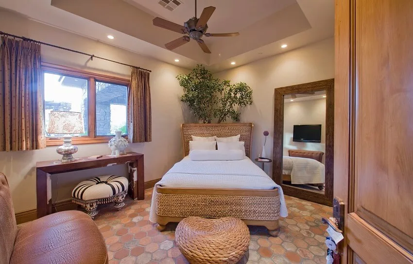 Bedroom with stone hexagon tile leather couch mirror leaned to a wall and rattan bed and ottoman