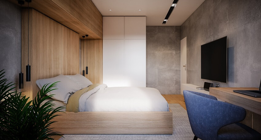 Bedroom with wood cabinets tv mounted to a concrete wall lighting fixtures blue armchair cozy bed indoor plant and wood floors