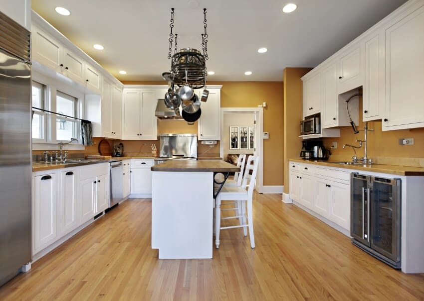 Big kitchen interior with white cabinets furniture metal appliances wooden floors and hanging storage for cooking pans