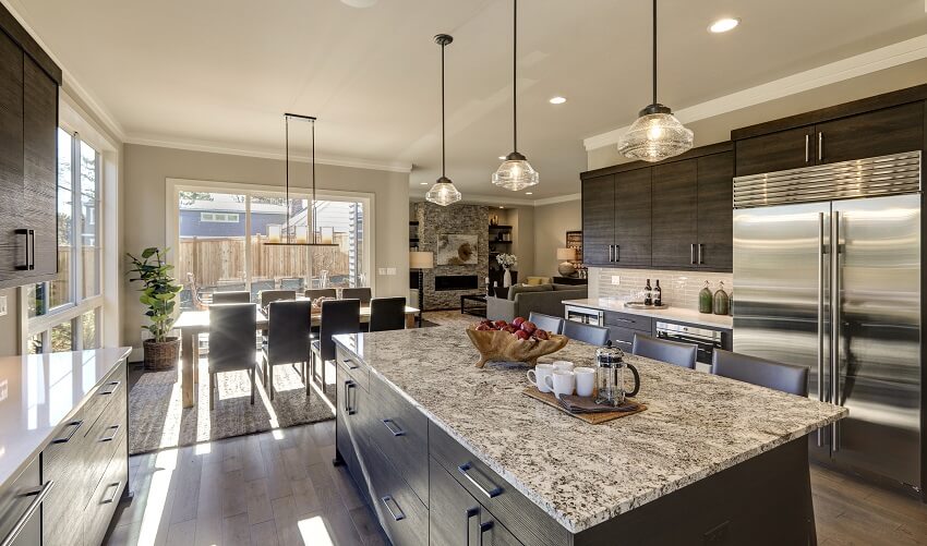 Bright kitchen with dark brown cabinets island with granite countertop and view of the dining area outdoor patio and living room with brick fireplace