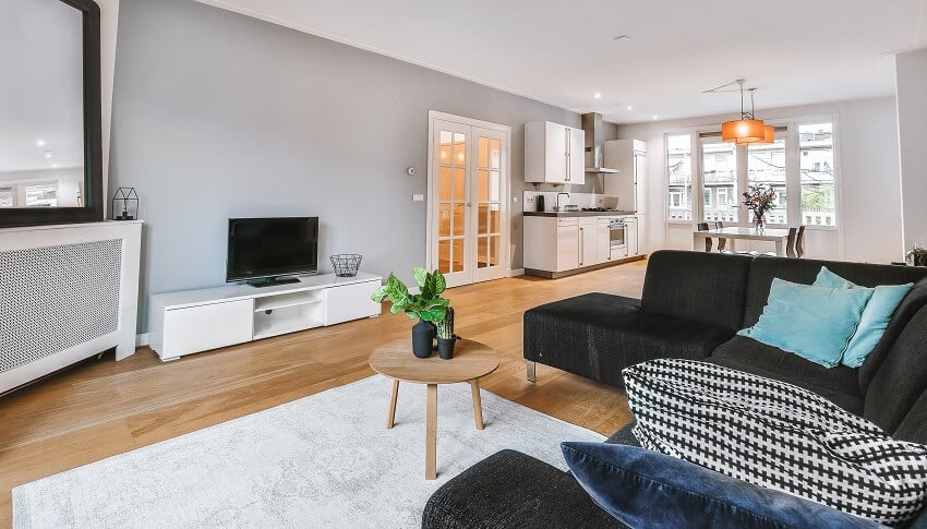 Bright room with black sofa, white carpet, grey walls and view of the kitchen and dining table