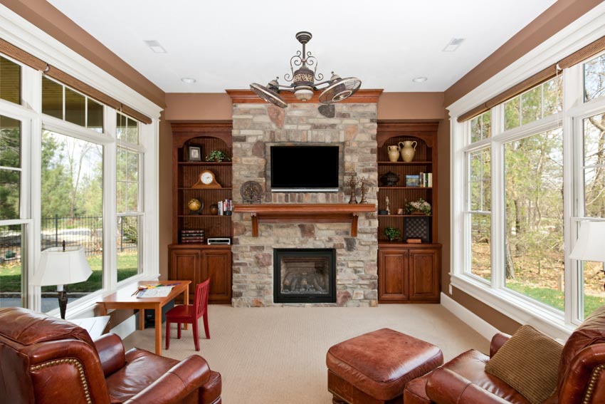 Classic living room brick fireplace mantel hanging light leather chair television shelves cabinets glass doors windows
