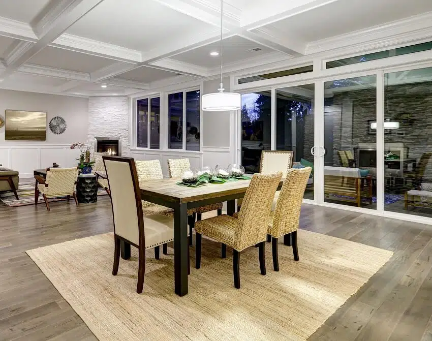 Dining and living room interior with wood floors coffered ceiling paneled walls floor to ceiling glass doors lead out to stunning covered patio area sofa and dining table with chairs