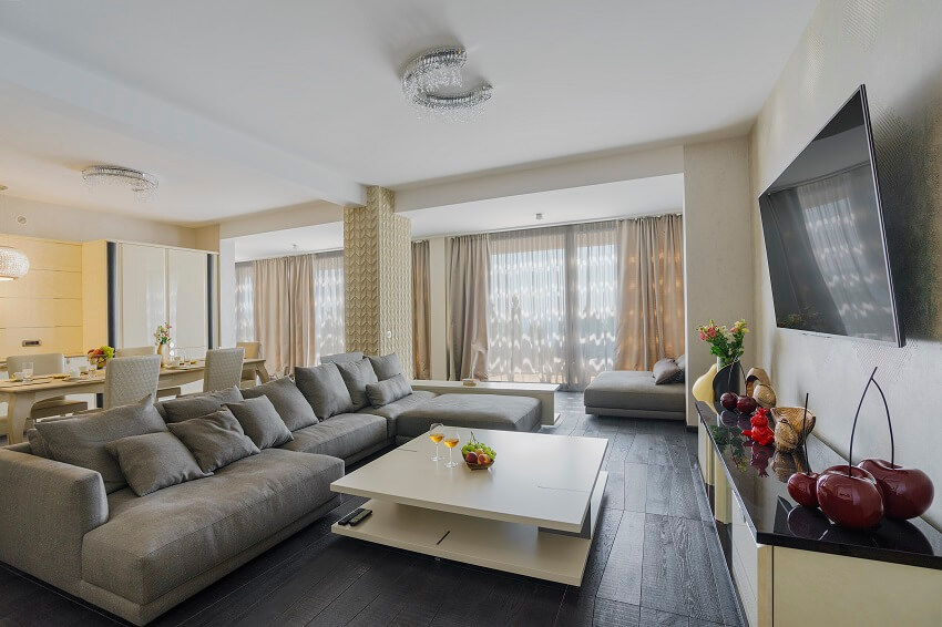 Dining and living room with large grey sofa white coffee table dining table cream colored curtains a column and dark wood floors