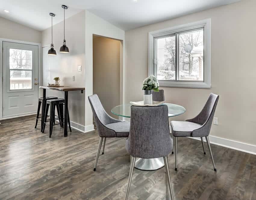 Dining area with dark wood floors round glass dining table grey chairs breakfast table attached to the wall with pendant lights and stools
