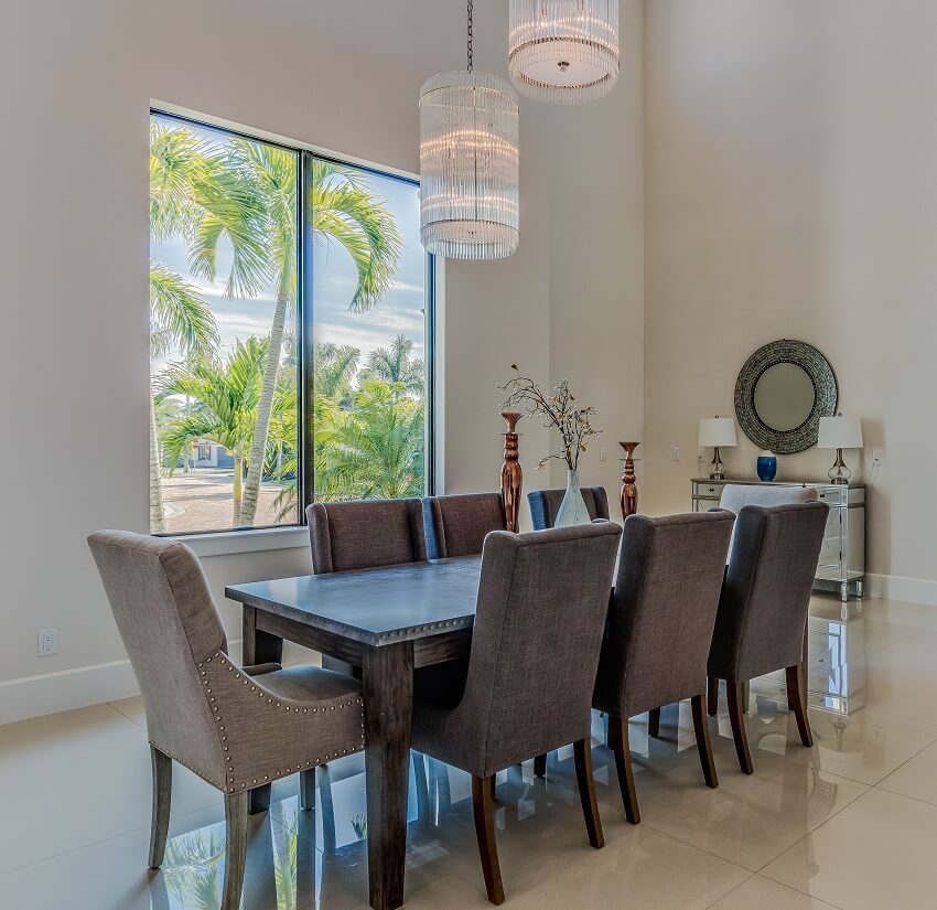 Dining room with high ceiling windows tile floors decors chandelier and dining table with grey chairs