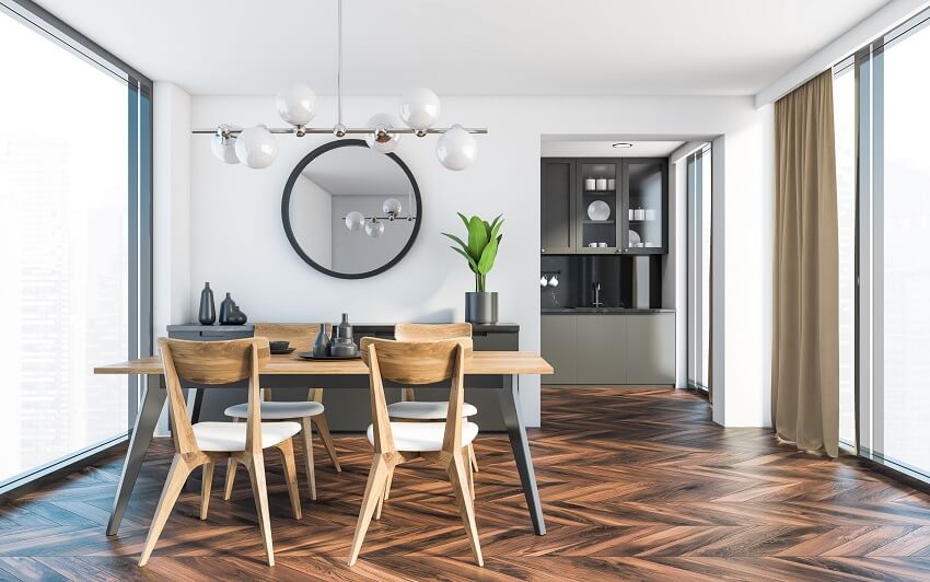 Dining room with white walls dark wooden floor panoramic windows long wooden table with chairs decors and kitchen in background