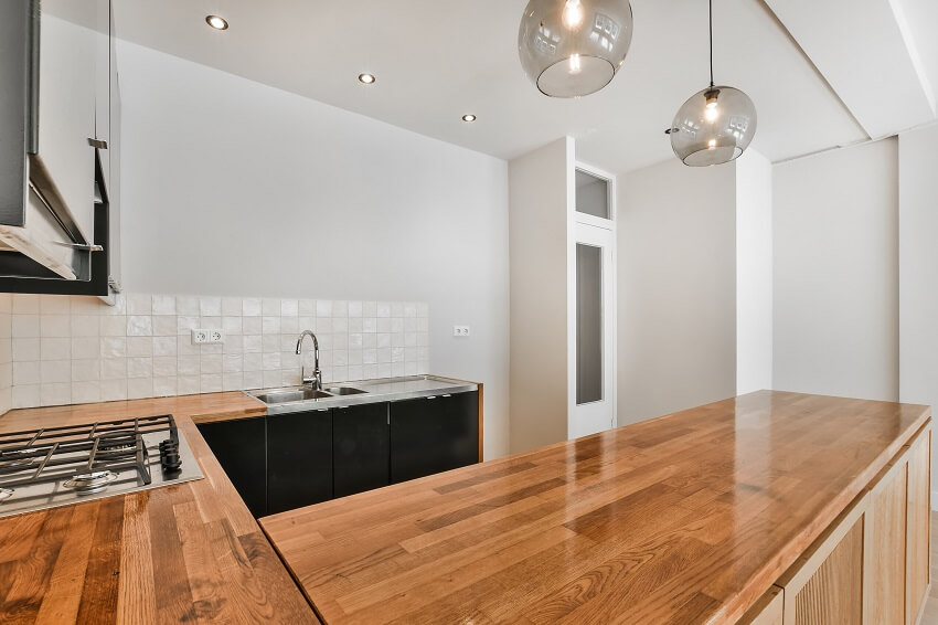 Kitchen with wood grain countertop, square backsplash and a cooktop